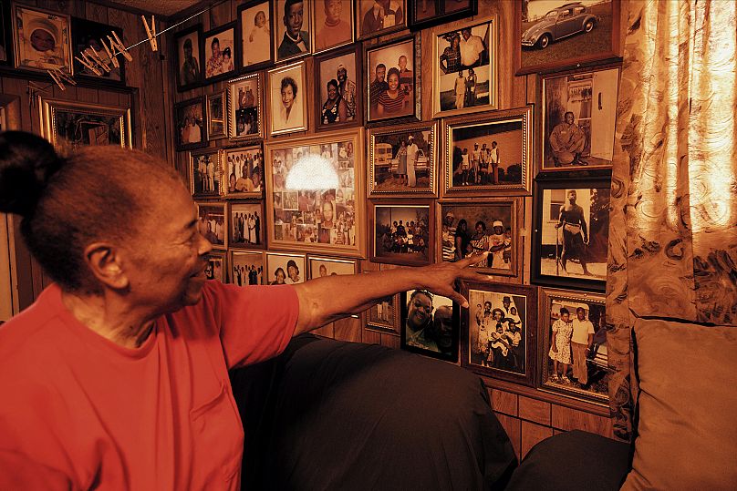 Pani Daisy wskazuje na fotografie wiszące na ścianie w jej domu.