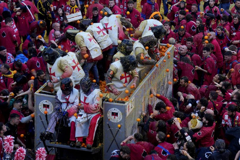 Ludzie noszący hełmy i kostiumy ochronne obrzucają się nawzajem pomarańczami podczas „Bitwy o Pomarańcze”." część obchodów karnawału w Ivrea we Włoszech.