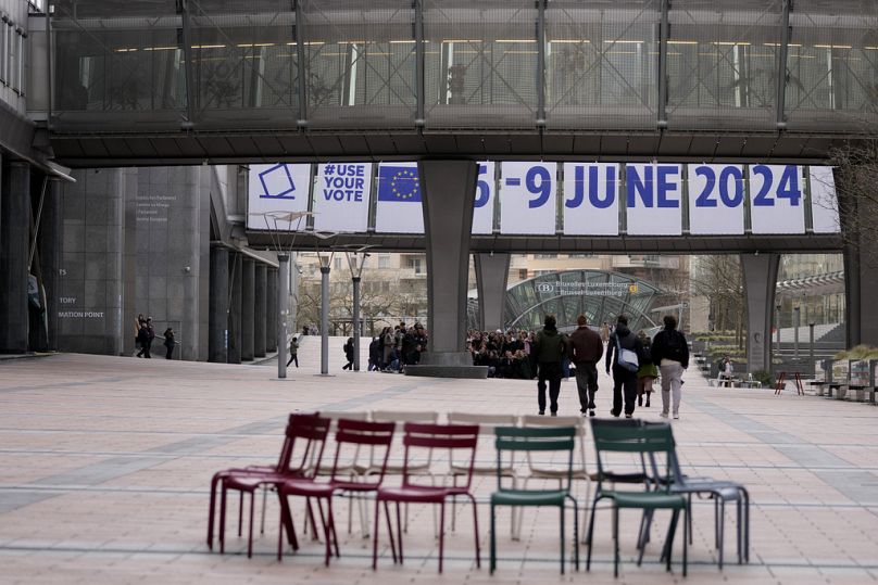 Ludzie gromadzą się przed banerem reklamującym wybory europejskie przed Parlamentem Europejskim w Brukseli, styczeń 2024 r