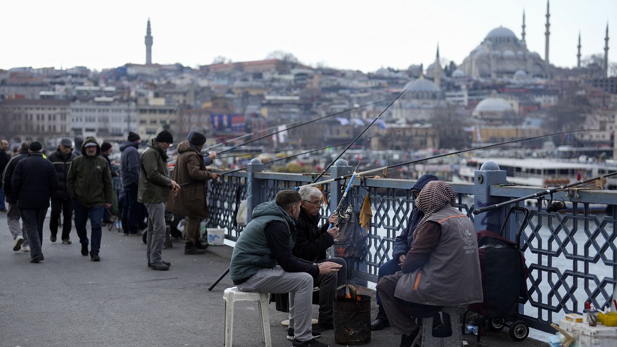 People warm themselves with a fire while fishing over the Galata bridge in Istanbul, Turkey. Feb. 21, 2024.