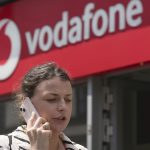 A woman talking on her mobile walks past a Vodafone store in London. June 14, 2023.