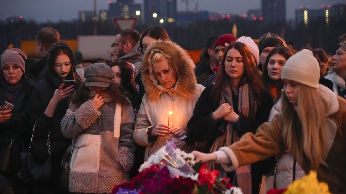 People lay flowers and light candles standing next to the Crocus City Hall, on the western edge of Moscow, Russia, Saturday, March 23, 2024.