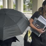 Celebrity handbag designer Nancy Gonzalez hides under an umbrella as she walks with her lawyer Andrea Lopez outside the federal courthouse Monday, April 22, 2024, in Miami.