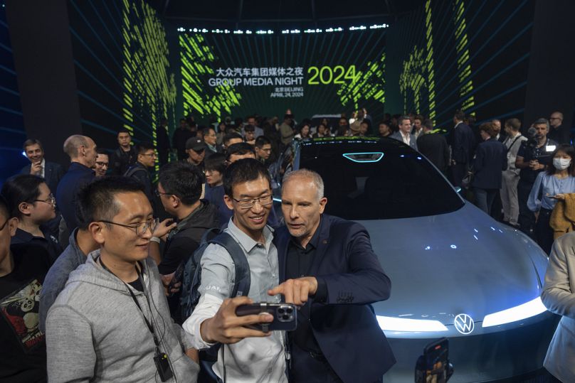 Uczestnicy pozują do zdjęć w pobliżu najnowszych samochodów zaprezentowanych podczas wydarzenia medialnego organizowanego przez Grupę Volkswagen podczas Salonu Samochodowego w Pekinie.