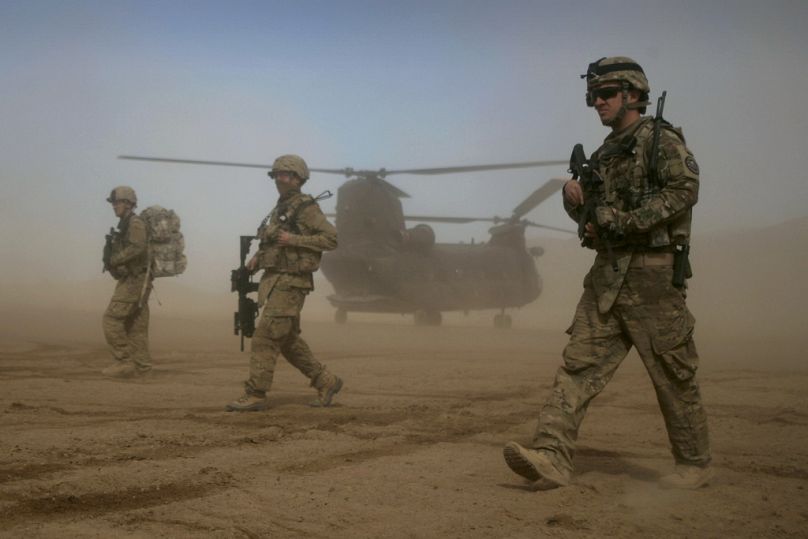 Żołnierze Międzynarodowych Sił Wsparcia Bezpieczeństwa (ISAF) pod dowództwem NATO idą, gdy w tle widać helikopter Chinook w Shindand, Herat, styczeń 2012 r.