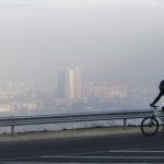 A man rides a bicycle along a road on the Vodno Mountain, with the town of Skopjes the Macedonian capital seen through polluted air in the background, Sunday, Nov. 8, 2015.