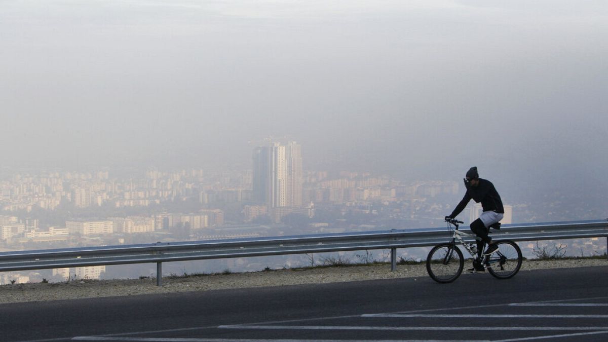 A man rides a bicycle along a road on the Vodno Mountain, with the town of Skopjes the Macedonian capital seen through polluted air in the background, Sunday, Nov. 8, 2015.