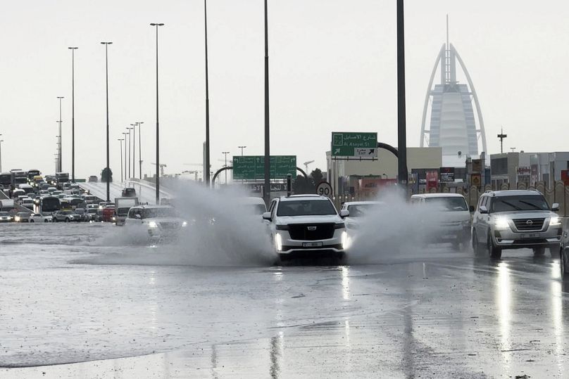 SUV rozpryskuje stojącą wodę na drodze w Dubaju, z luksusowym hotelem Burj Al Arab w tle.  w Dubaju
