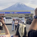 Visitors take a photo in front of a convenient store at Fujikawaguchiko town, Japan, with a backdrop of Mount Fuji