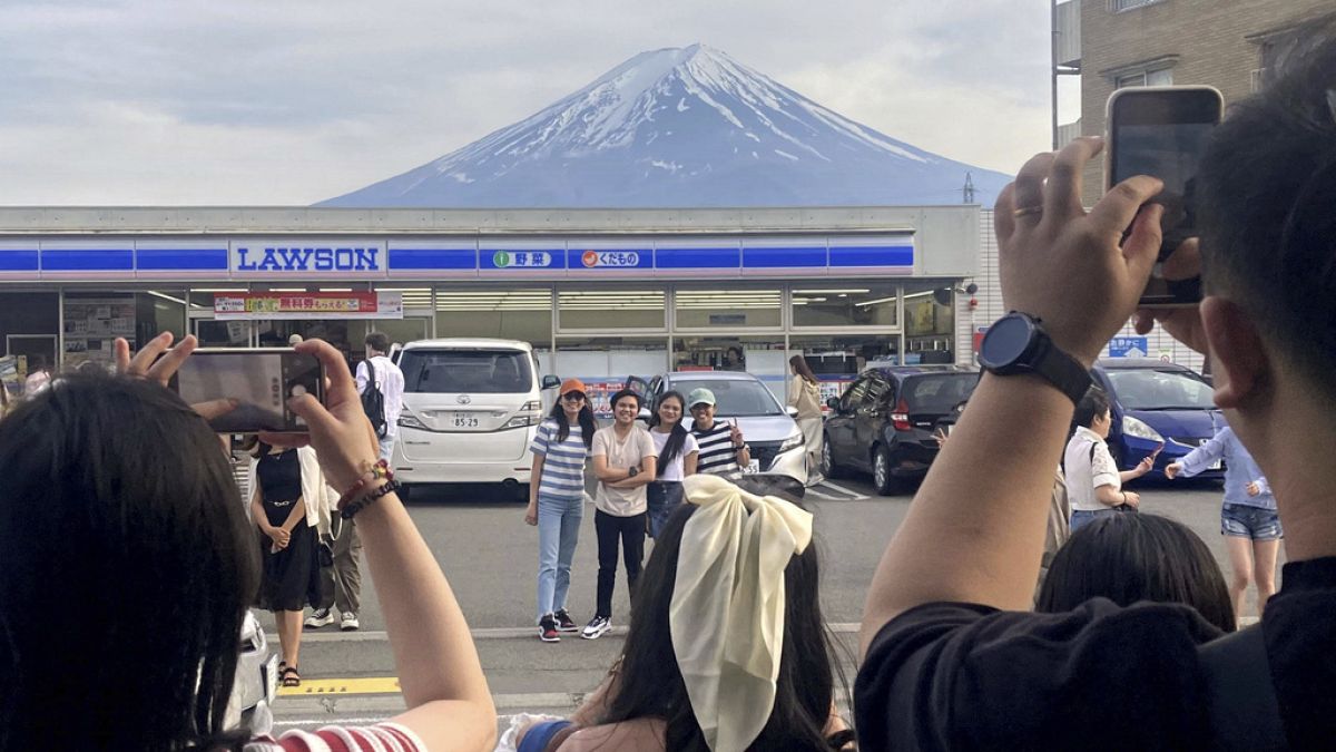 Visitors take a photo in front of a convenient store at Fujikawaguchiko town, Japan, with a backdrop of Mount Fuji