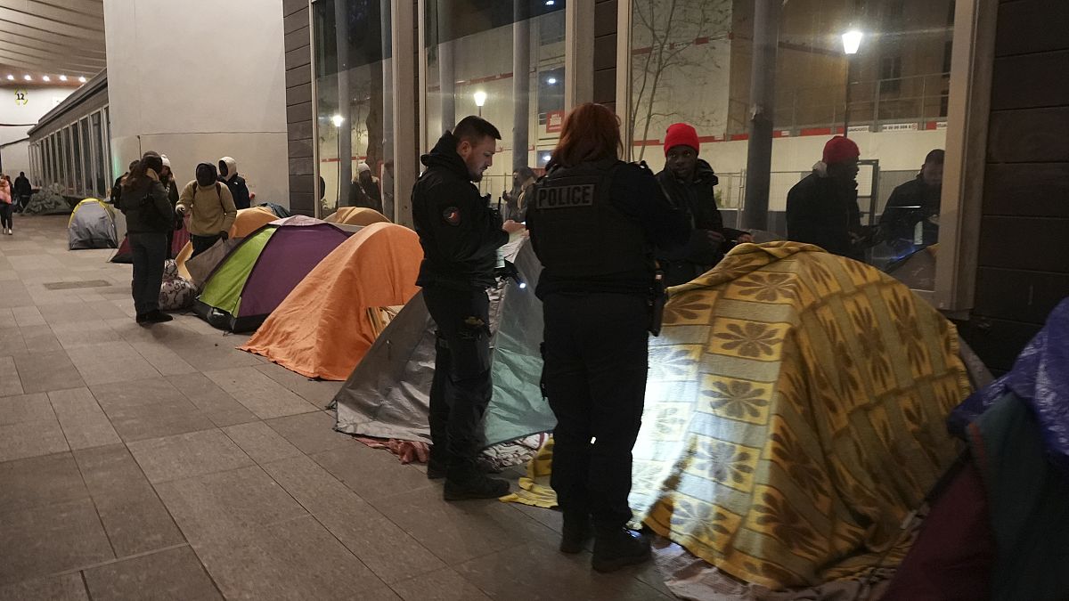 Police officers check a migrant in a makeshift camp, early Tuesday, April 23, 2024 in Paris.