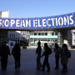 A group stands under an election banner outside the European Parliament in Brussels on April 29, 2024.