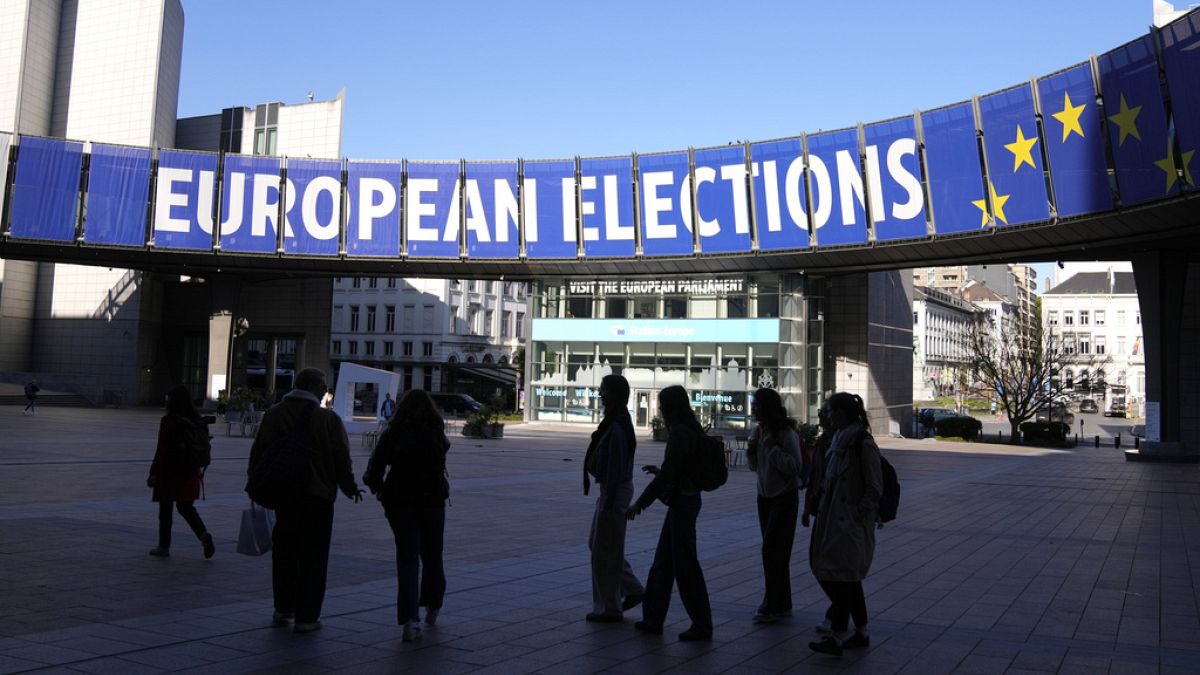 A group stands under an election banner outside the European Parliament in Brussels on April 29, 2024.