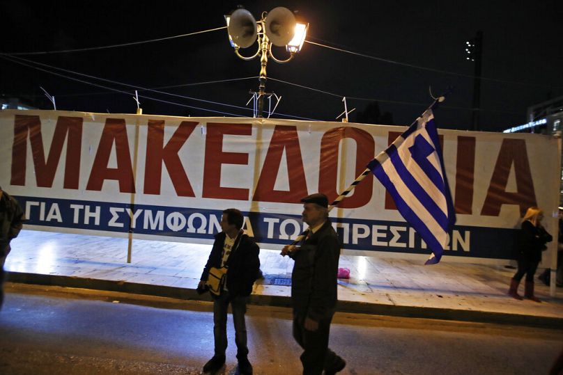 Przeciwnik porozumienia z Prespy trzyma grecką flagę i stoi przed plakatem podczas wiecu przed greckim parlamentem, styczeń 2019 r.