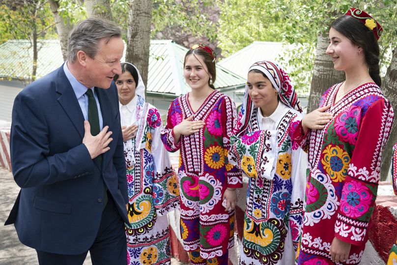 Minister spraw zagranicznych Wielkiej Brytanii David Cameron zostaje powitany przez kobiety w tradycyjnych strojach podczas wizyty w projekcie hydroelektrycznym Nurek, około 70 km na południe od Duszanbe, 22 kwietnia 2024 r.