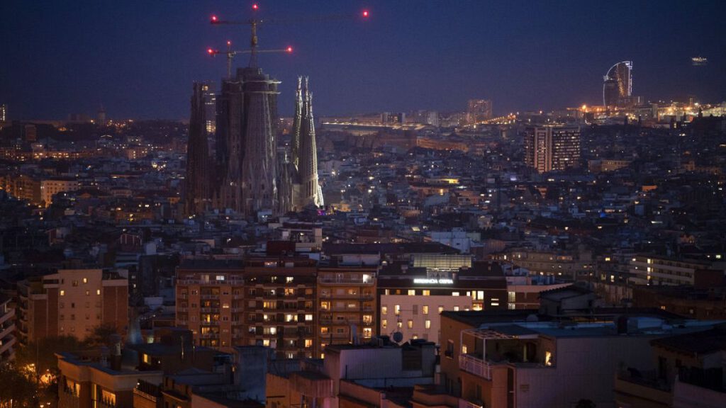 FILE - Buildings and La Sagrada Familia basilica are illuminated at night in Barcelona, Spain, Wednesday, March 18, 2020.