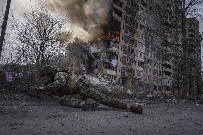   Ukraiński funkcjonariusz policji kryje się przed płonącym budynkiem, który został uderzony podczas rosyjskiego nalotu w Awdijiwce na Ukrainie, piątek, 17 marca 2023 r.