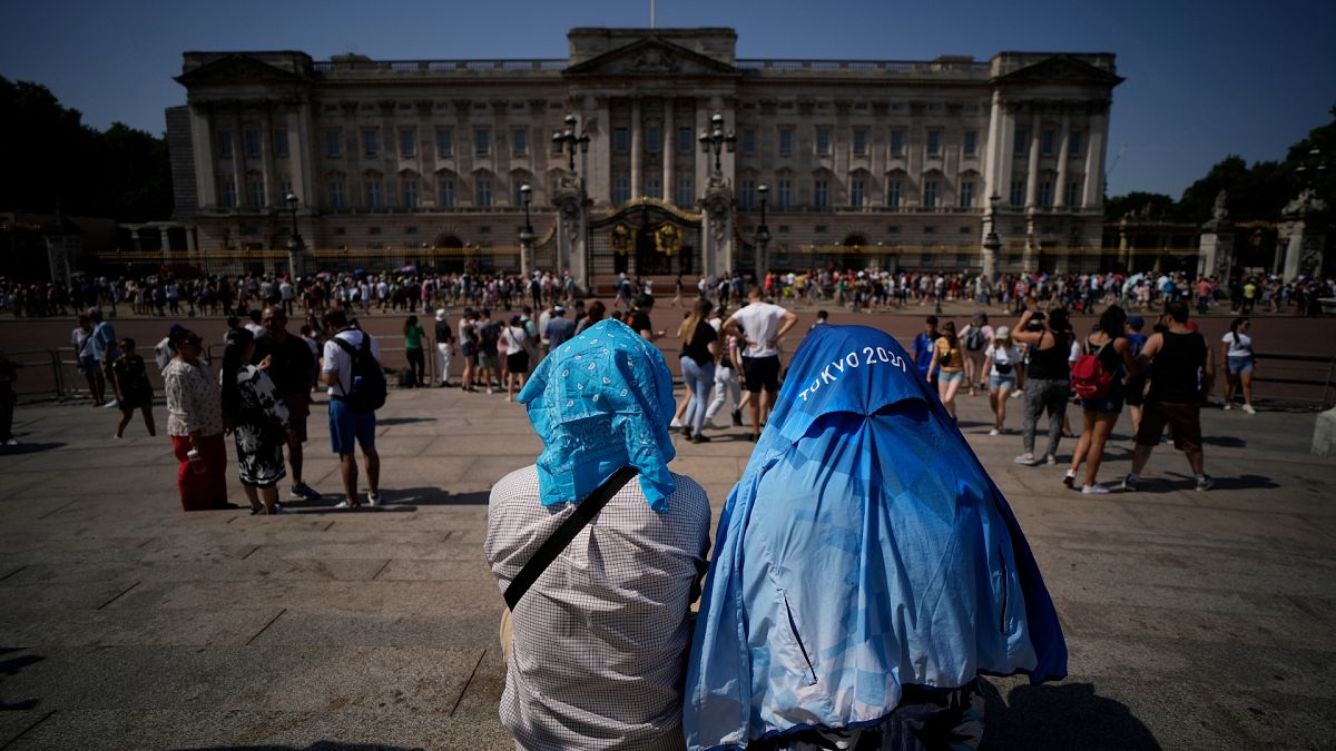 People sit covering their heads from the sun outside Buckingham Palace in the 2022 heatwave.