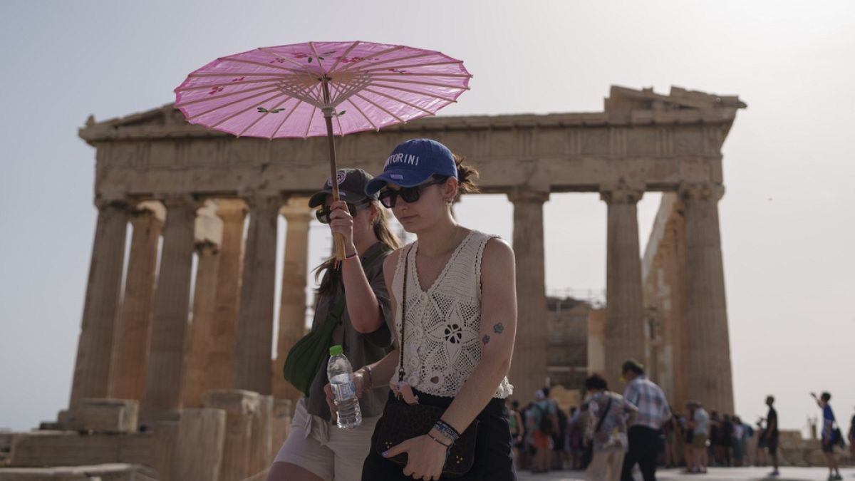 Tourists shelter from the heat with an umbrella walk at the Parthenon at the ancient Acropolis in central Athens during June - the hottest June on record