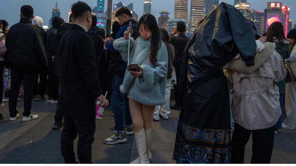 A woman looks at her phone on a selfie stick on the bund, a historic riverside district of Shanghai known for its Western architecture on March 18, 2024.