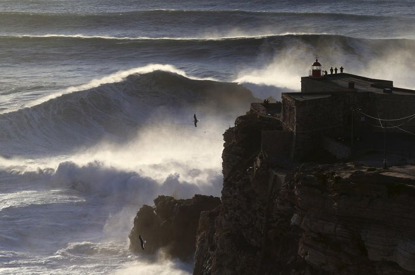 Ludzie na szczycie latarni morskiej w Nazare obserwują, jak fale rozbijają się podczas sesji surfingu na dużych falach na Praia do Norte, czyli plaży północnej w Nazare, luty 2017 r.