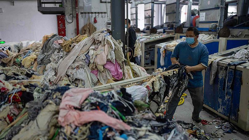 Pracownik wrzuca zużyte tekstylia do niszczarki w Wenzhou Tiancheng Textile Company, jednym z największych chińskich zakładów recyklingu bawełny w Wenzhou we wschodnich Chinach