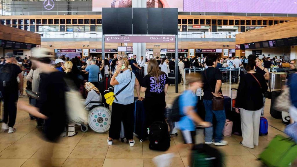 Numerous passengers wait in front of a black display board at the capital