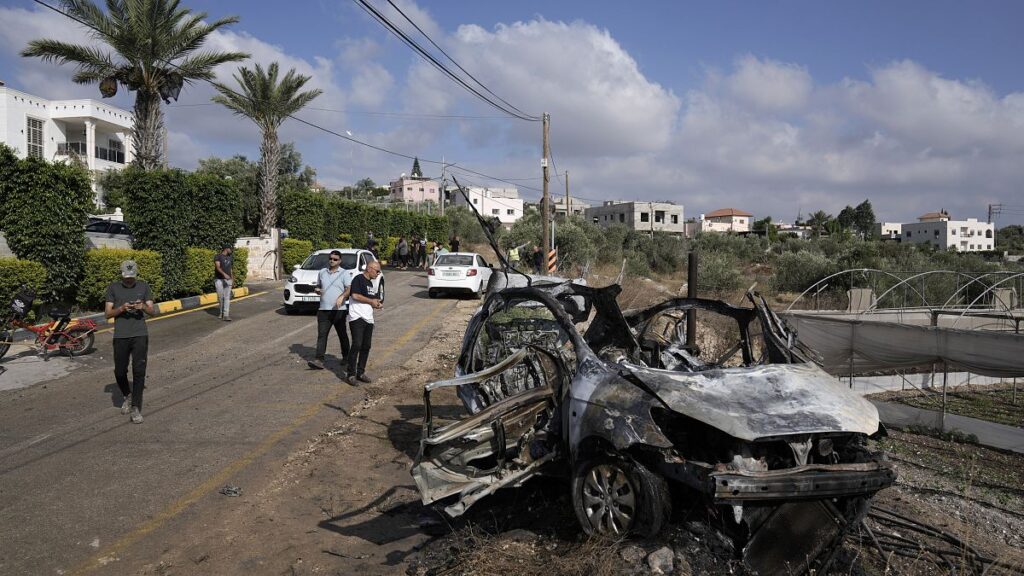 Palestinians gather around a car destroyed in a drone strike Zeita village, north of the West Bank city of Tulkarem.