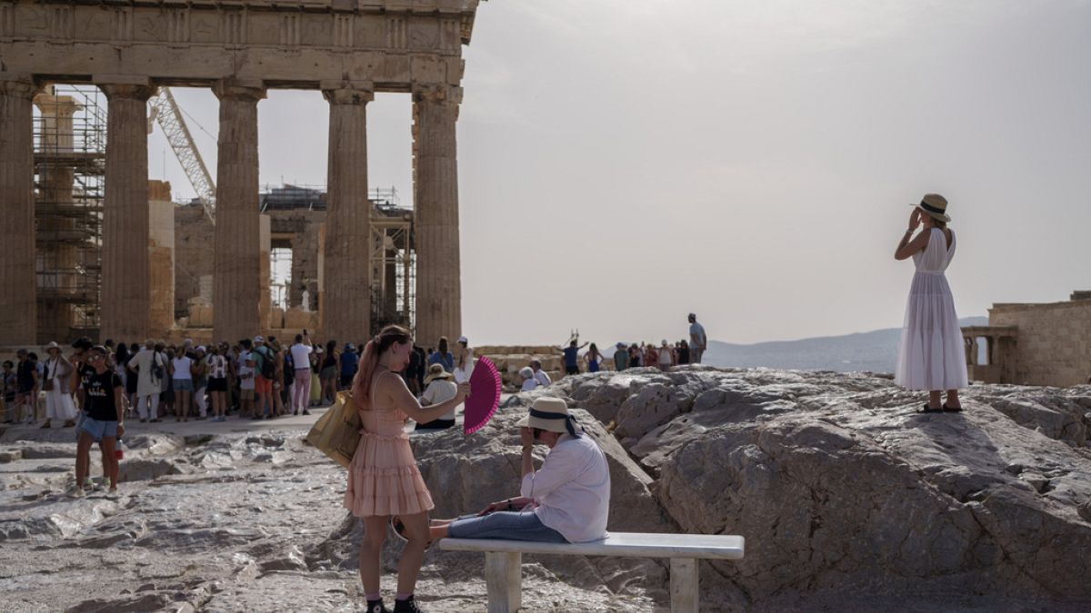 A tourist uses a hand fan to cool down another one sitting on a bench in front of the Parthenon at th Acropolis in Athens as the country suffers months-long extreme heat