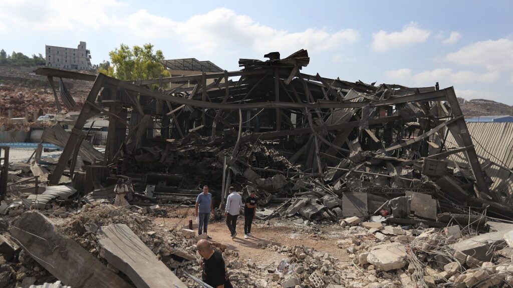 People walk at an industrial area destroyed by an Israeli airstrike, in Wadi al-Kfour, Nabatieh province, south Lebanon. 17 August 2024.