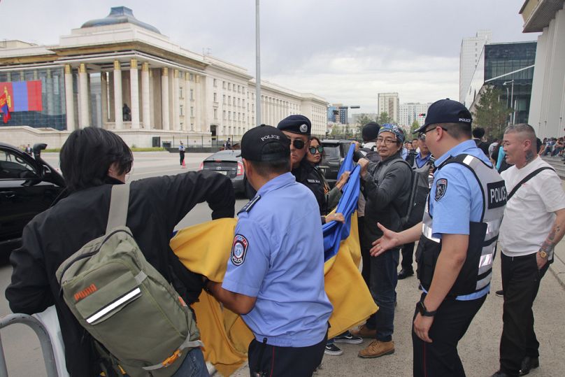 Policja i funkcjonariusze służb bezpieczeństwa w Ułan Bator uniemożliwiają członkom grupy protestującej przeciwko wojnie niesienie flagi ukraińskiej podczas wizyty Władimira Putina.