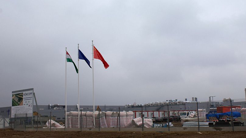 Widok placu budowy na obrzeżach Debreczyna. Powiewają flagi Węgier, Unii Europejskiej i Chin.