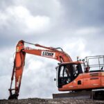 An orange construction excavator digging on an overcast day