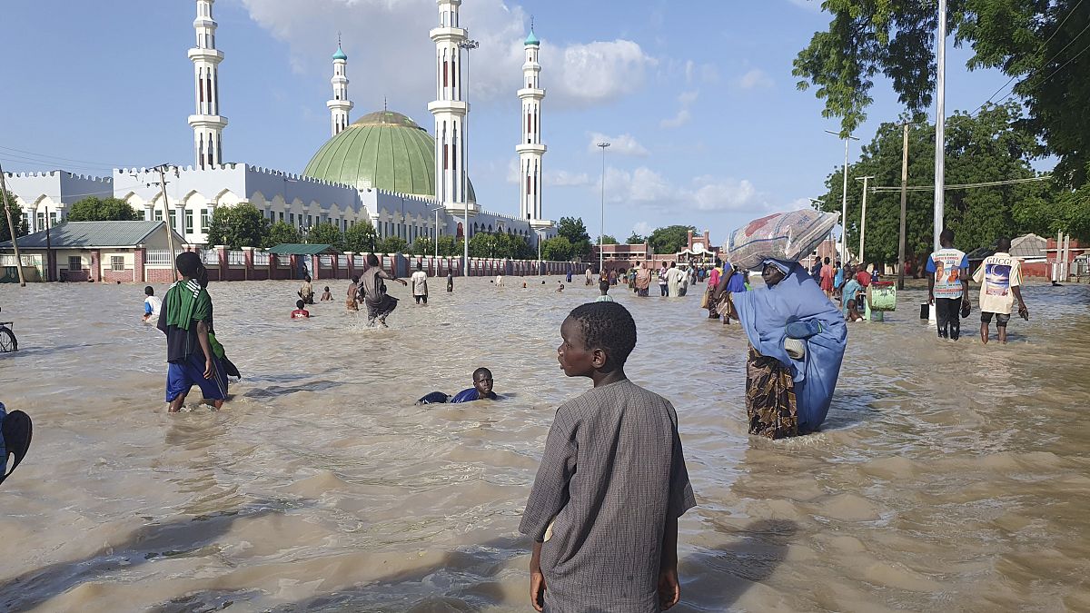 People walk through floodwaters following a dam collapse in Maiduguri, Nigeria, Tuesday Sept 10, 2024.