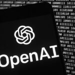 The OpenAI logo appears on a mobile phone in front of a computer screen with random binary data, Thursday, March 9, 2023, in Boston.