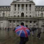 A woman with an umbrella stands in front of the Bank of England, at the financial district in London, , Nov. 3, 2022.