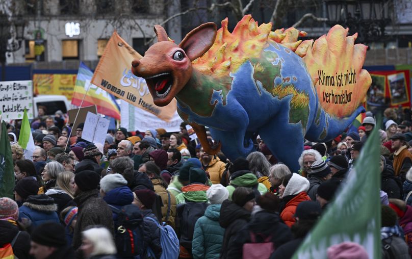 Ludzie stoją wokół postaci przedstawiającej płonący kangur z kontynentami i napisem 