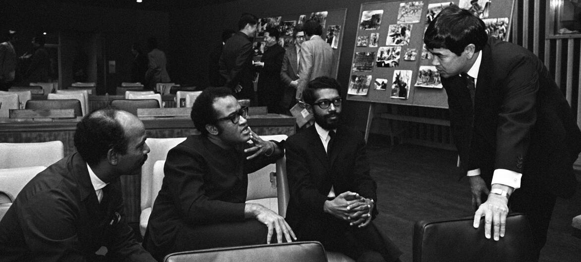 Członkowie komitetu dekolonizacyjnego ONZ, w tym przedstawiciele FRELIMO Sharfuddine M. Khan i Jorge Rebelo, Salim A. Salim z Tanzanii i Thomas Tanaka, rozmawiają w sali konferencyjnej wyposażonej w pokazy zdjęć.