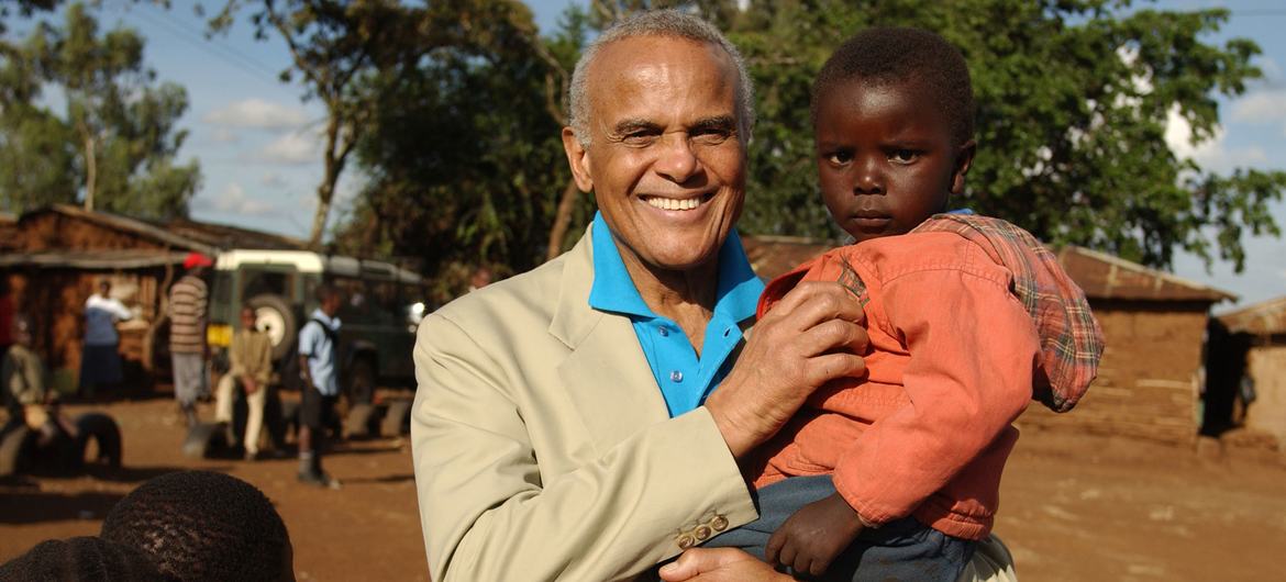 Ambasador Dobrej Woli UNICEF Harry Belafonte trzyma małe dziecko stojąc z innymi dziećmi w Kiberze w Nairobi w Kenii.