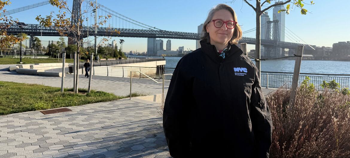 Kathryn Prybylski stoi na brukowanej promenadzie nadbrzeżnej w ramach projektu East Side Coastal Resiliency na Manhattanie, mając za sobą most Manhattan Bridge i East River.