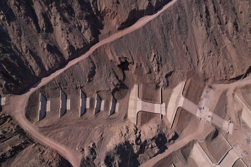 Widok z lotu ptaka na nowo wybudowaną betonową zaporę przeciwpowodziową i serię basenów osadowych w suchych górach Chile.