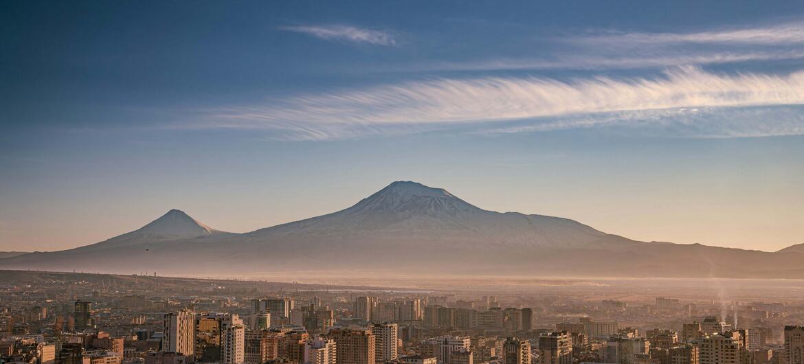 Panorama powietrzna Erewania w Armenii, z gęstymi budynkami mieszkalnymi na pierwszym planie i ośnieżoną górą Ararat wznoszącą się z tyłu pod czystym niebem.